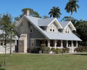 A grey house with a stone chimney on a clear day