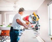 A man with a saw cutting some planks of wood inside a house that is under renovation